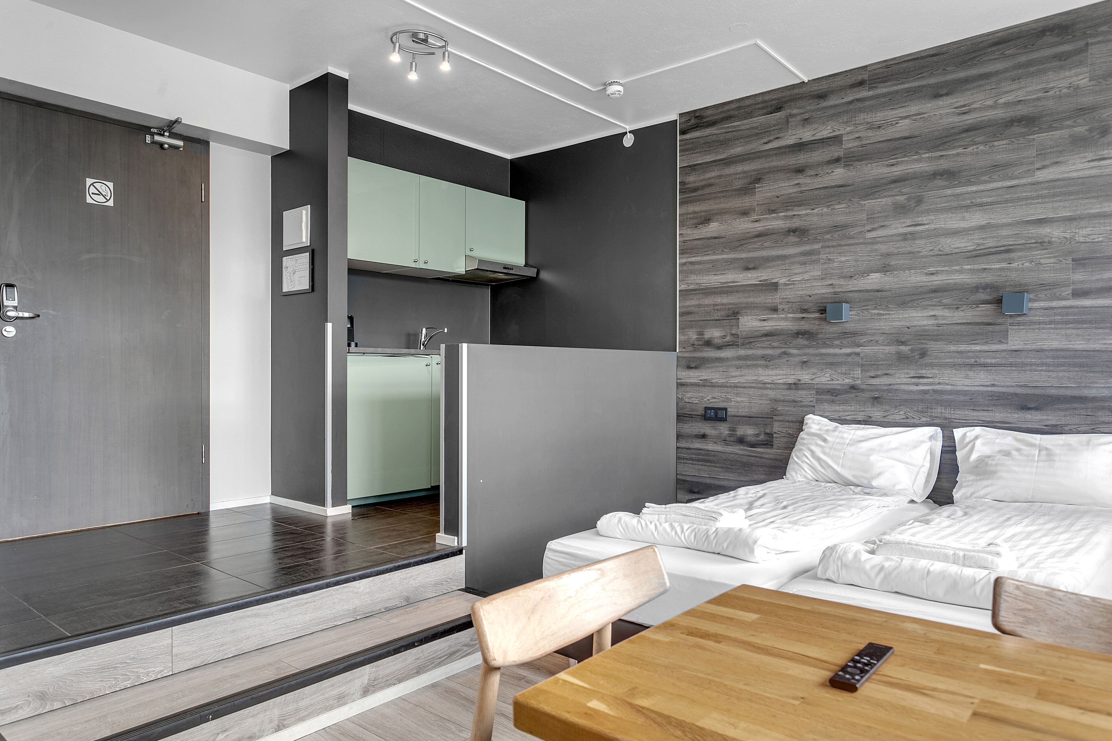 Een moderne hotelkamer met een houten vloer, een slaapbank, een houten eettafel, en een keuken met een inbouwoven en kastjes.