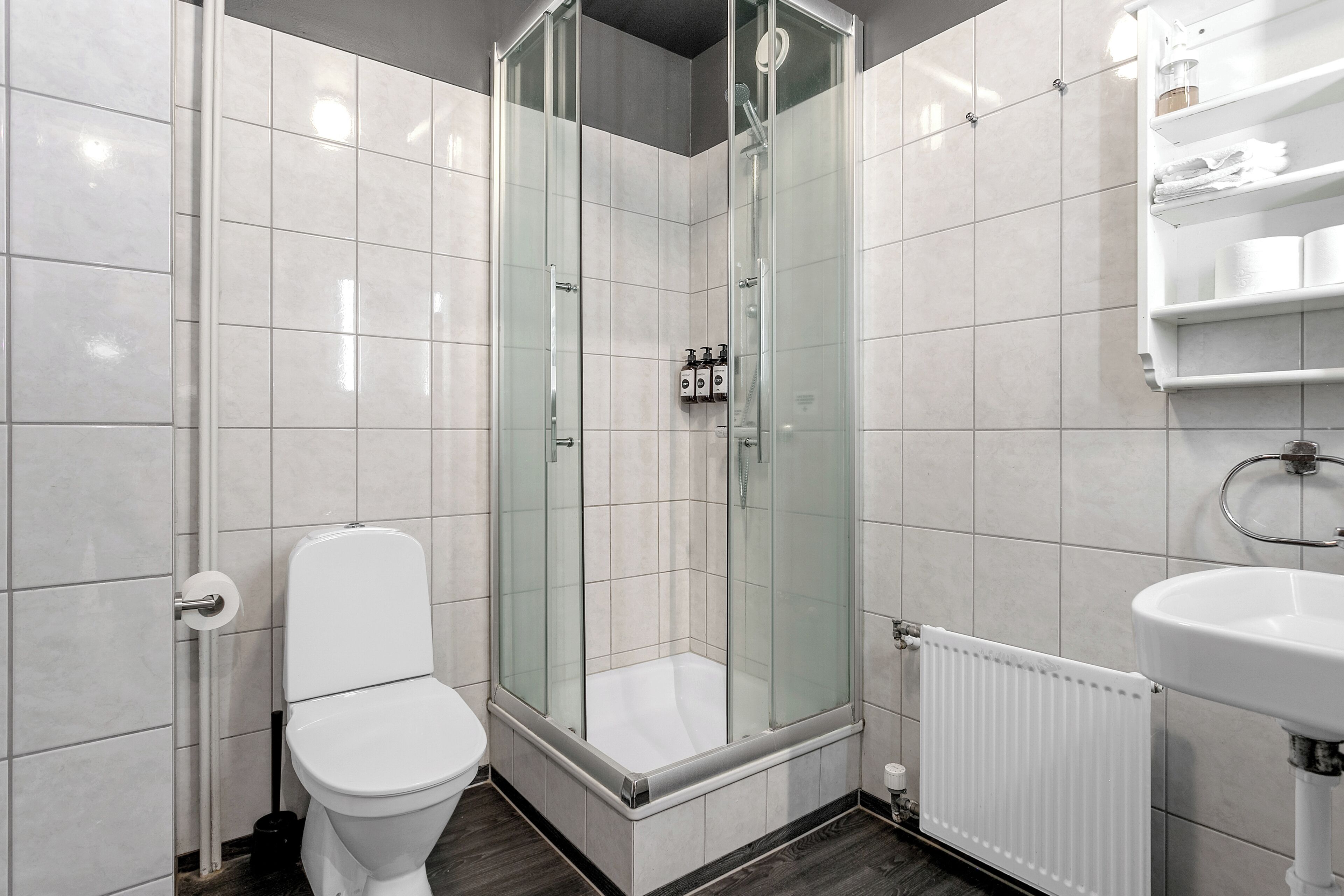 Un bany modern amb dutxa tancada amb vidre, un vàter blanc i un lavabo blanc.