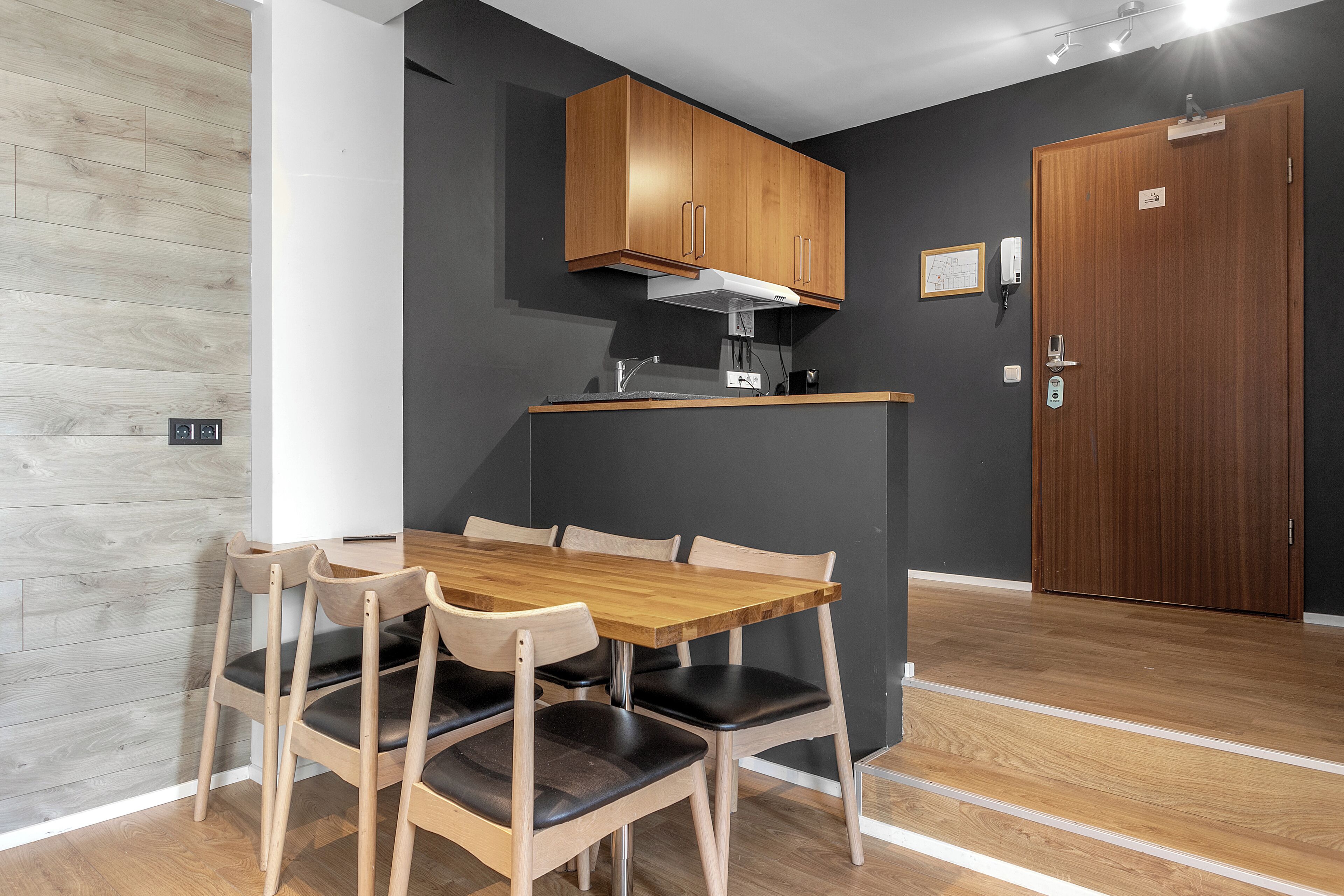 A compact kitchen with wooden cabinets, a built-in stove, and a dining area with a wooden table and chairs.