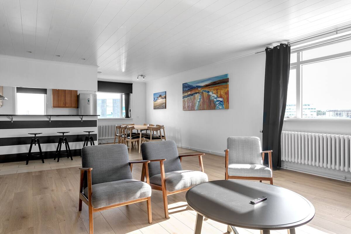 A modern living room with a dining area, large windows, and artwork on the walls.