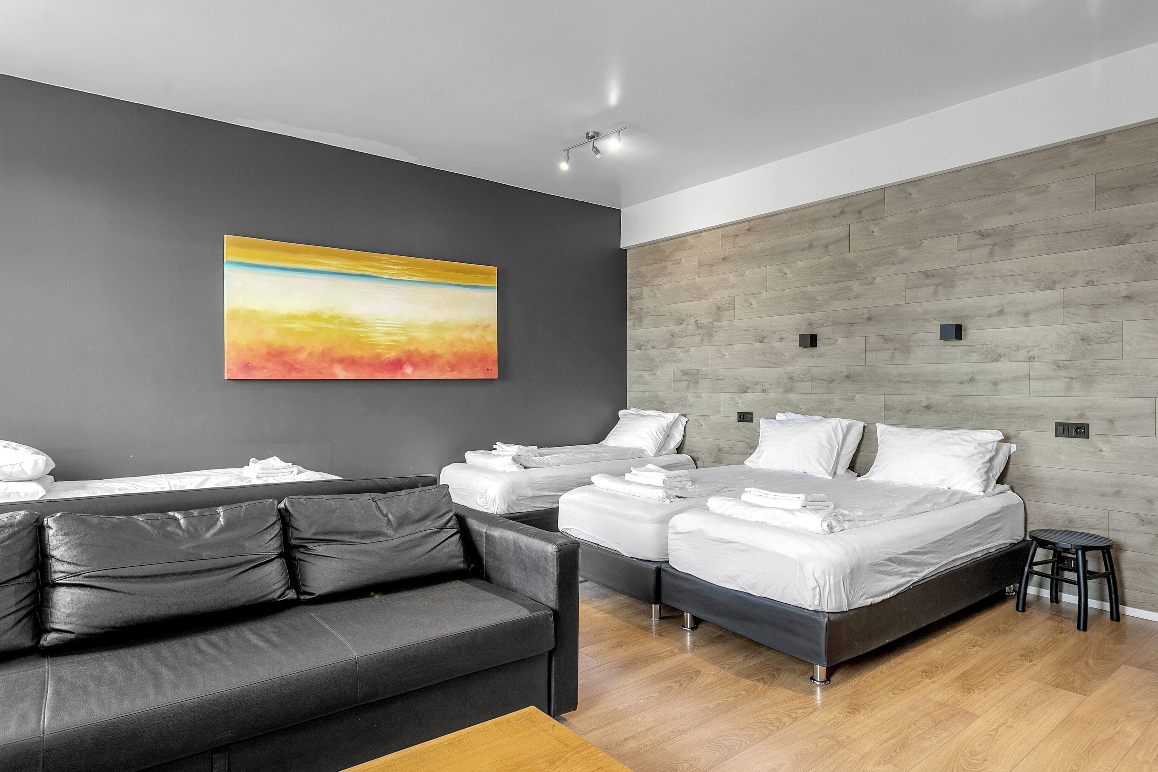 Une chambre d’hôtel moderne aux tons de gris et de blanc, comprenant un canapé, deux lits, un mur décoratif en bois et un tableau.