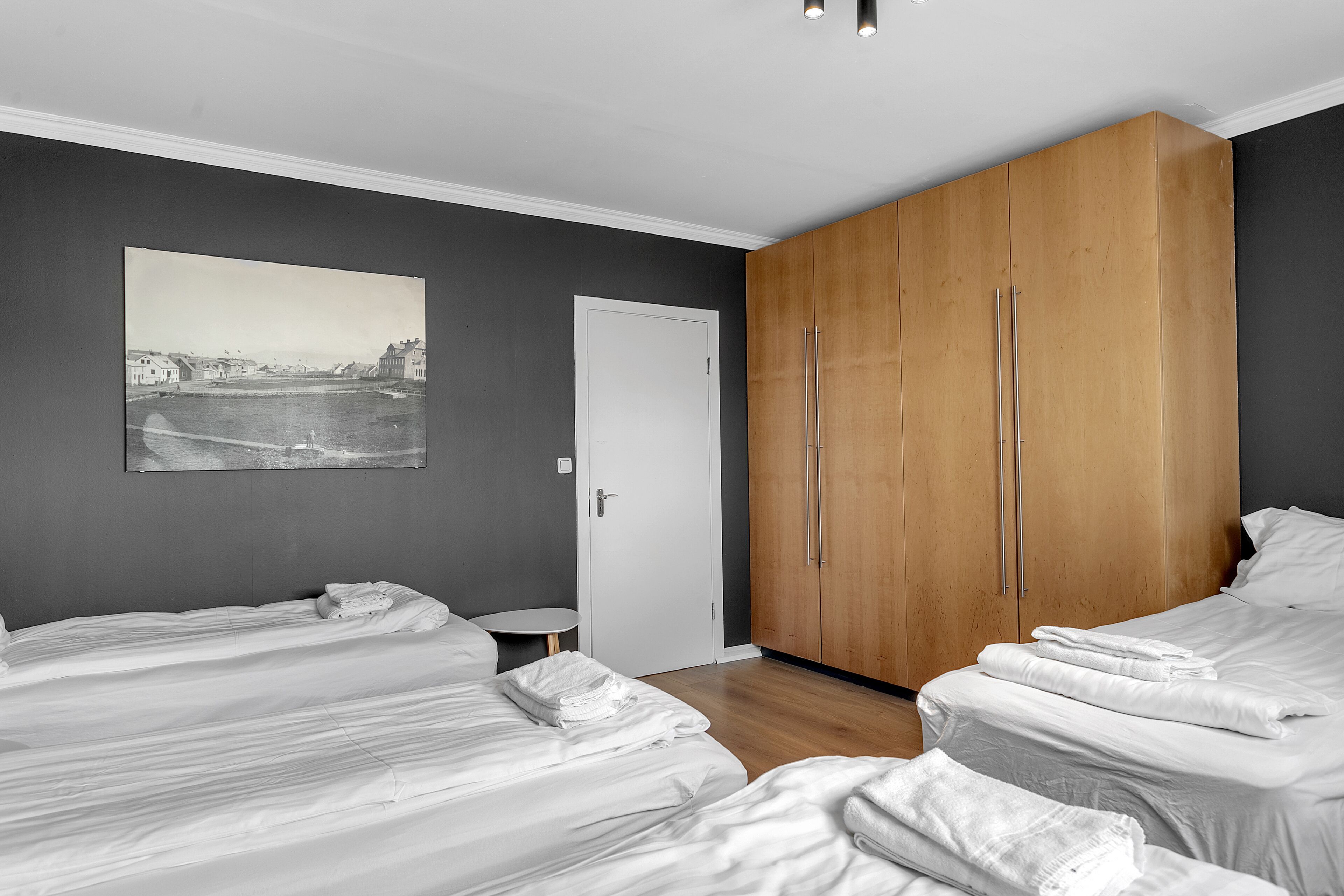 Una camera d'albergo con due letti, un armadio in legno, un tavolino rotondo e un quadro appeso al muro.