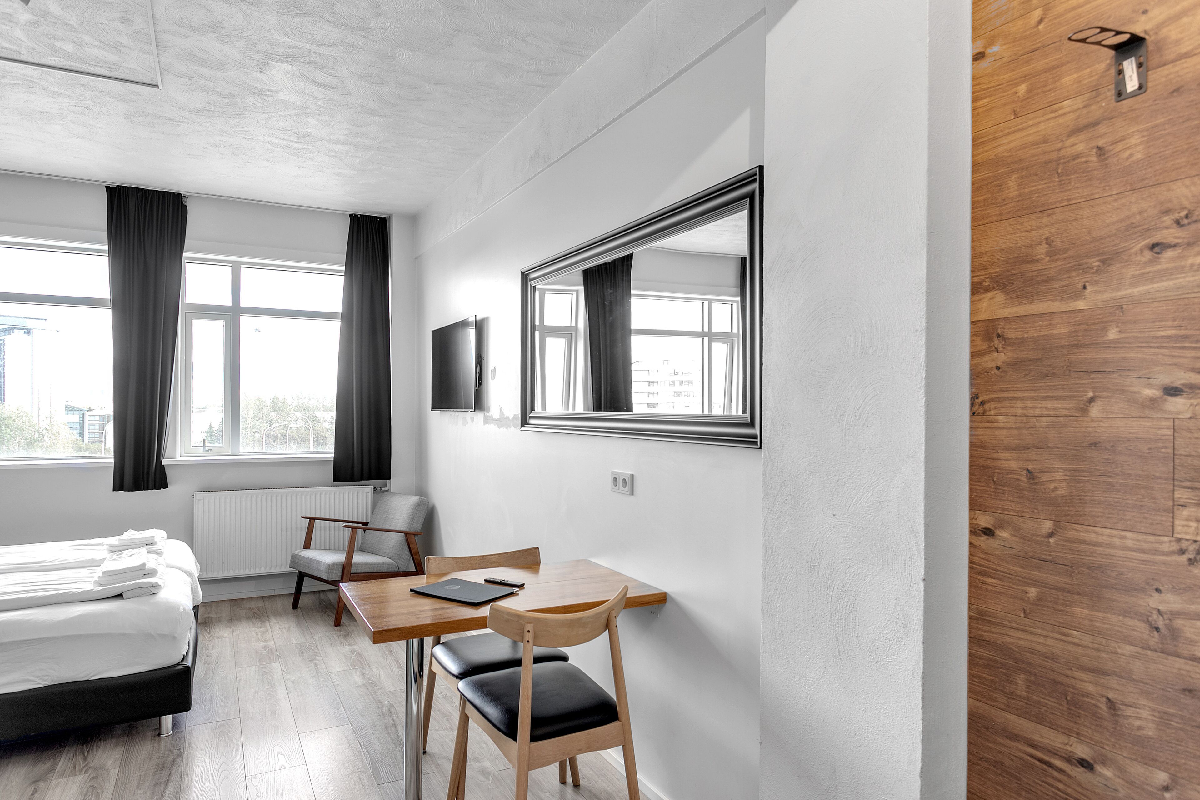 A modern hotel room with a bed, a desk, a chair, and a large mirror.