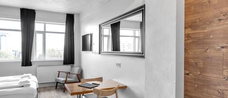 A modern hotel room with a bed, a desk, a chair, and a large mirror.