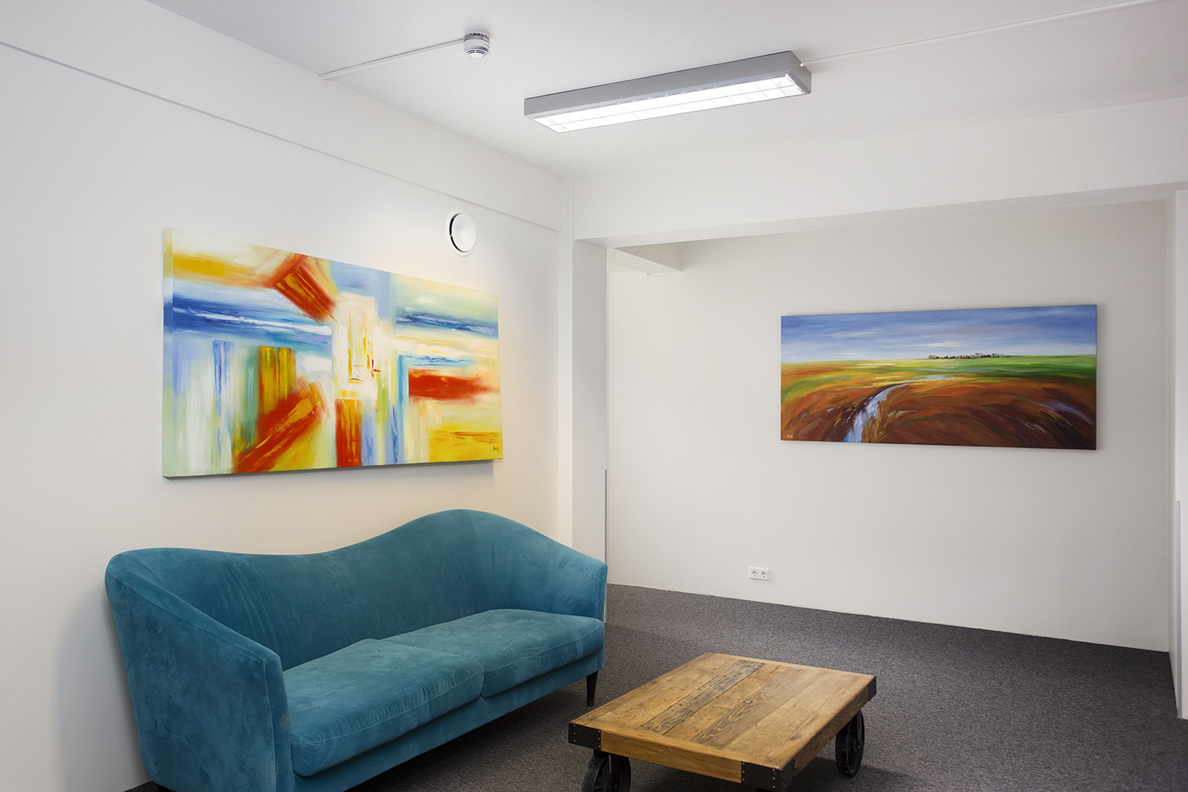 A room with a blue sofa, a wooden coffee table, and two paintings on the walls.
