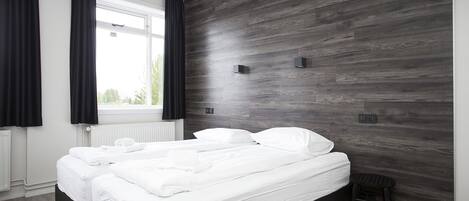 A modern bedroom with a large bed, a small stool, and a window with curtains.