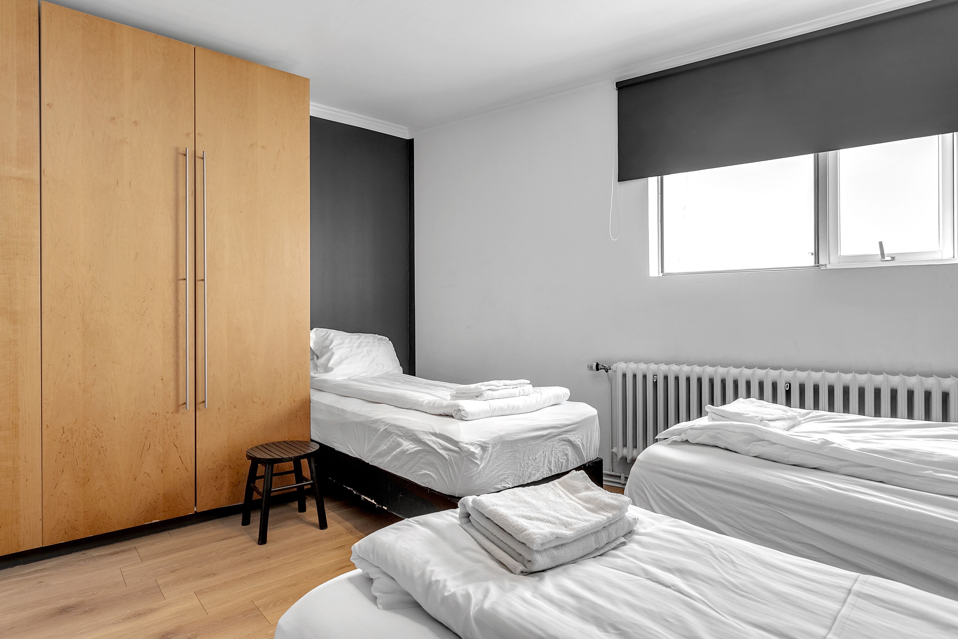 A modern bedroom with two beds, a wooden wardrobe, and a radiator.