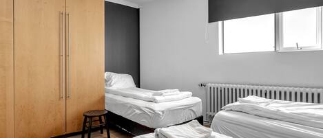 Un dormitorio moderno con dos camas, un armario de madera y un radiador.