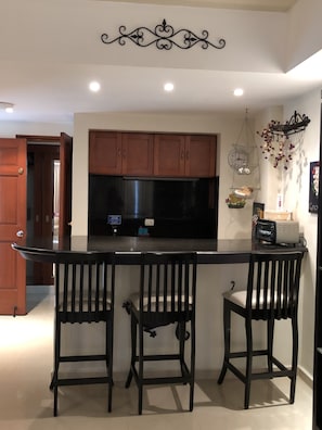 Kitchen features a central island with a countertop and barstools, wooden cabinets, and a stainless steel refrigerator.