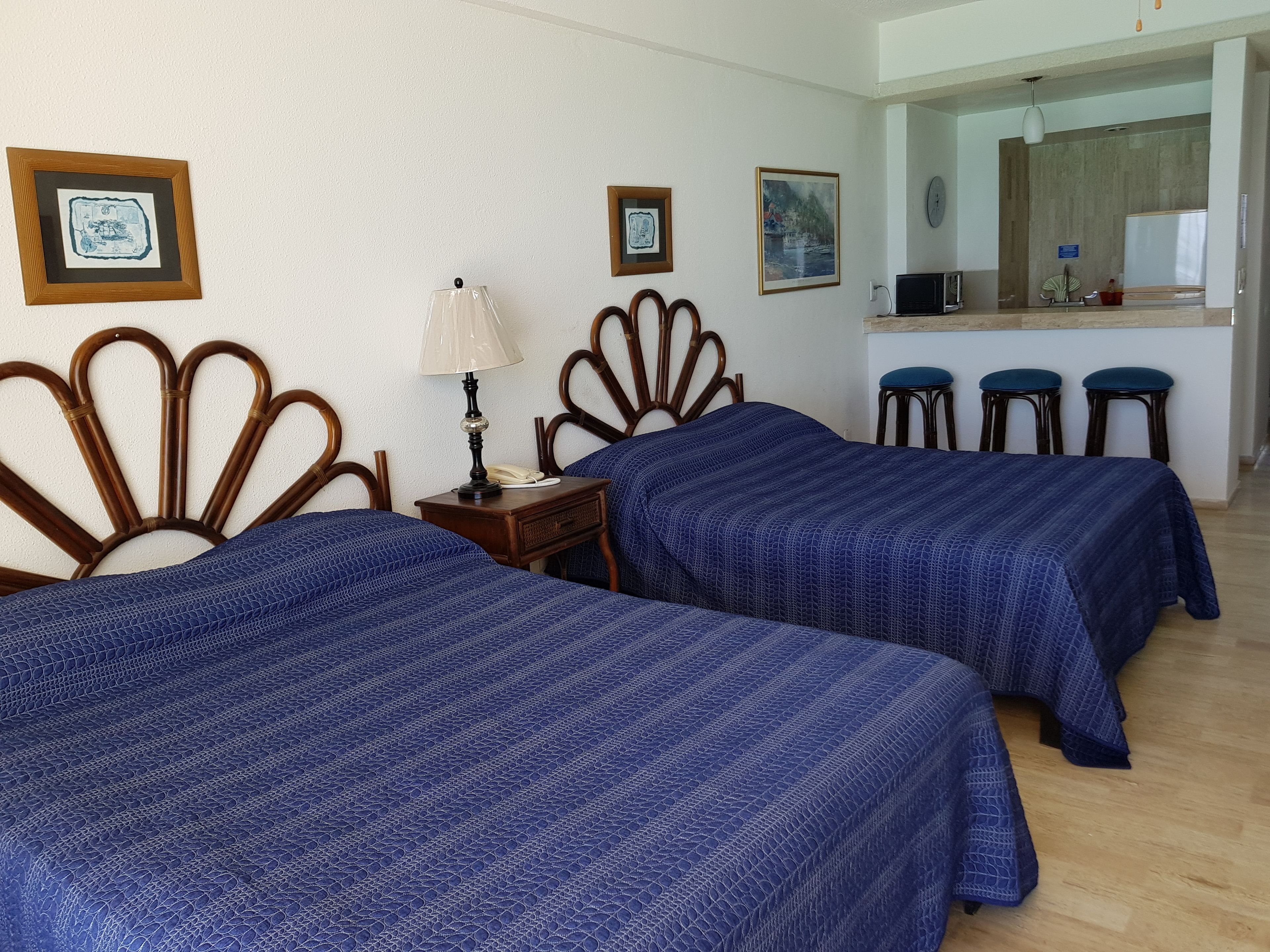 A hotel room with two beds, a desk with a lamp, and a kitchenette area.