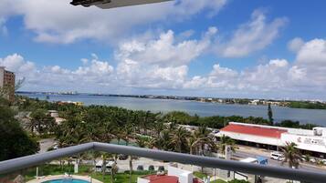 A view from a balcony overlooking a swimming pool, a body of water, and a distant cityscape.