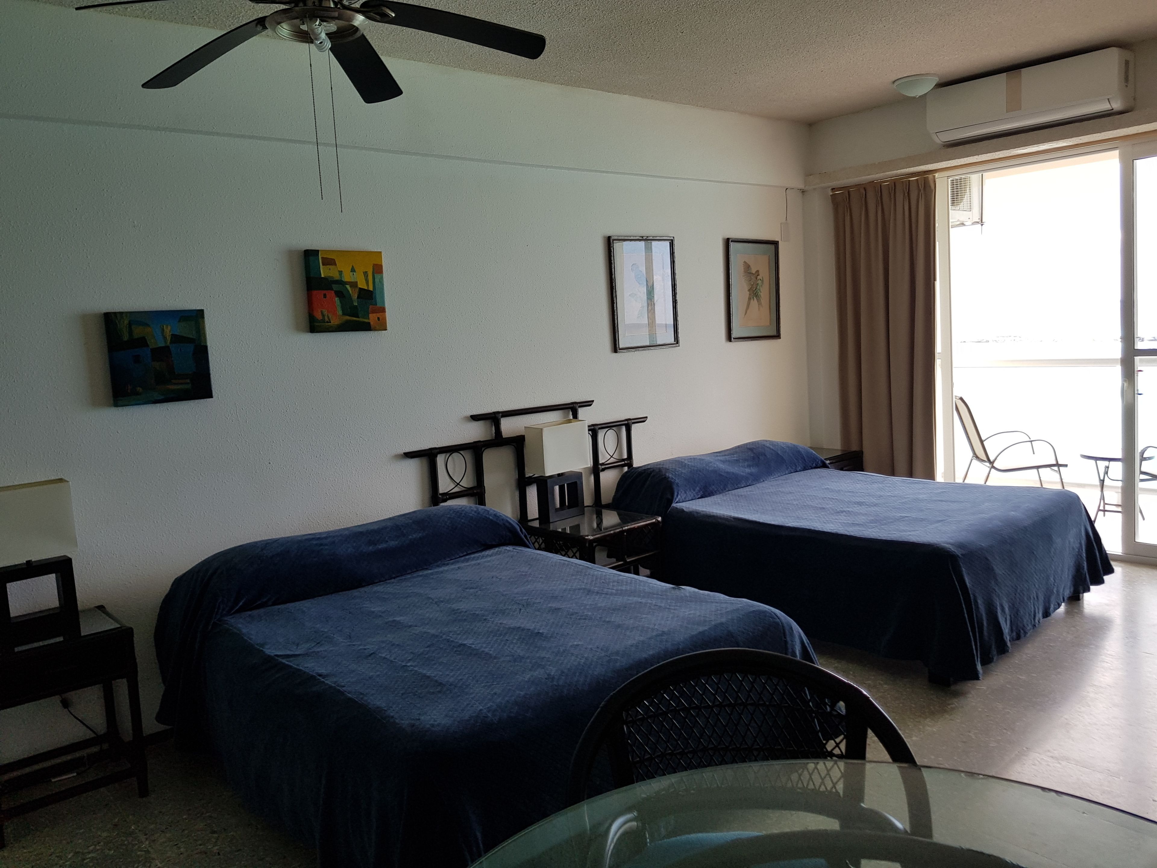 Une chambre d’hôtel avec deux lits, un ventilateur de plafond, une table et une chaise.