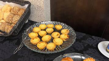 Une table sur laquelle se trouvent une assiette en verre remplie de tartelettes aux œufs et un panier de petits pains.