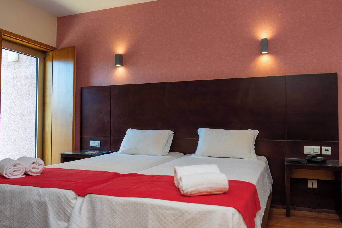 A hotel room with two beds, a red blanket, and two white pillows.