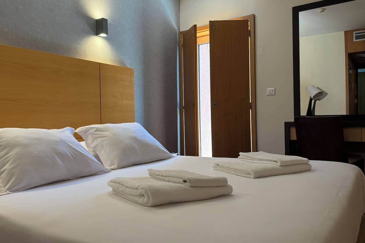 A hotel room with a neatly made bed, two pillows, and folded towels.