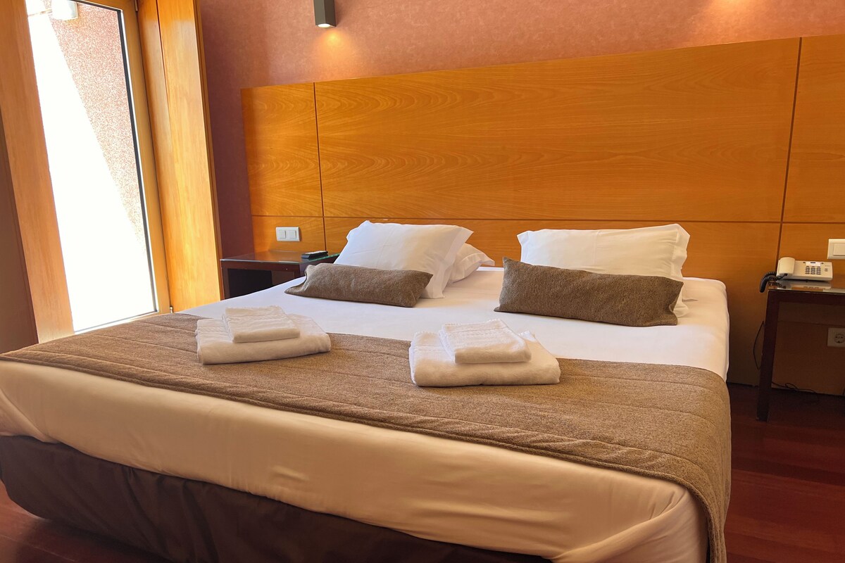 A hotel room with a large bed, wooden headboard, white linens, and two bedside tables with lamps.
