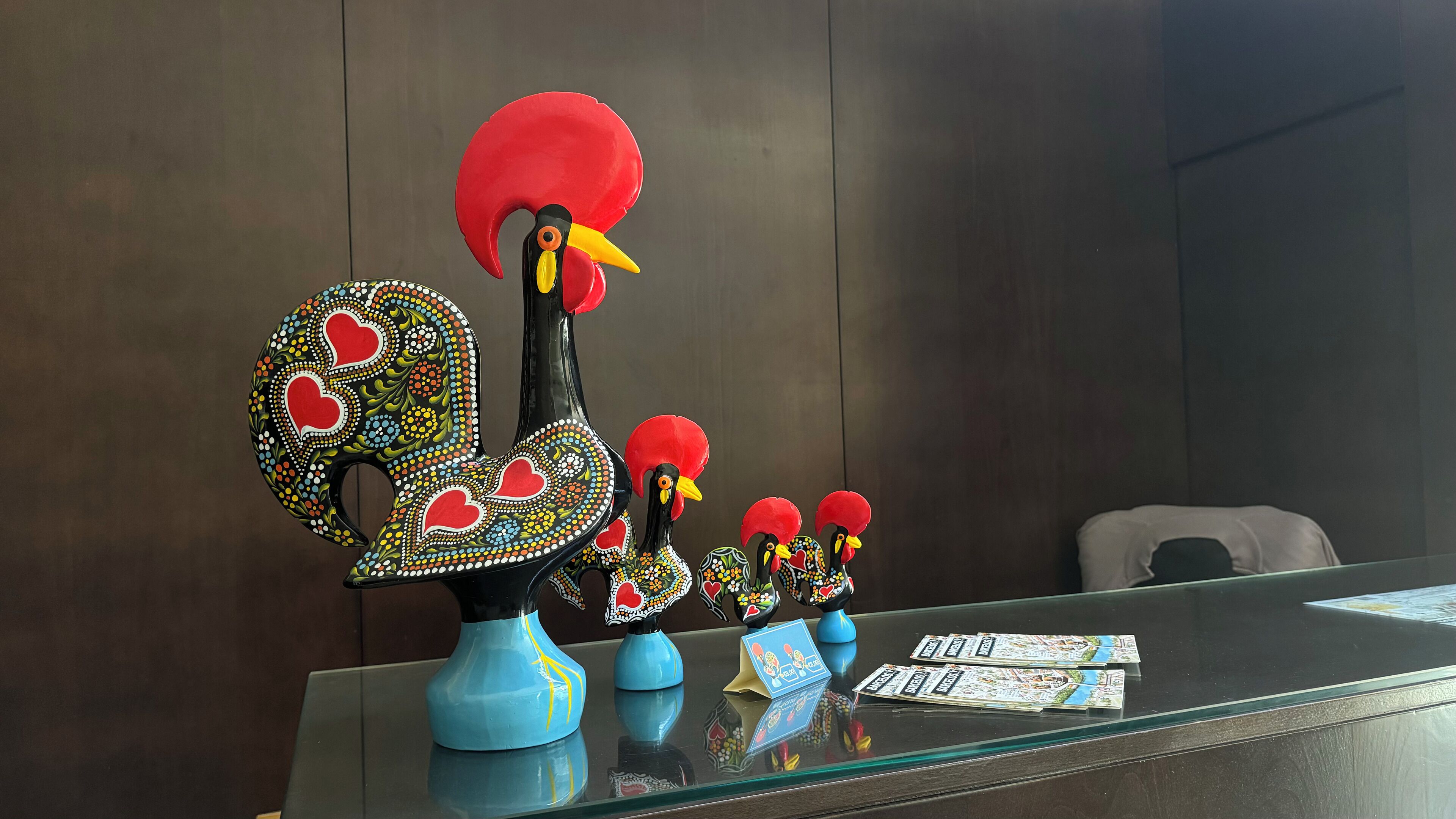 Uma receção com figuras de galos de cerâmica decorativas e uma vitrine de vidro.