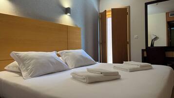 A hotel room with a neatly made bed, two pillows, and folded towels.