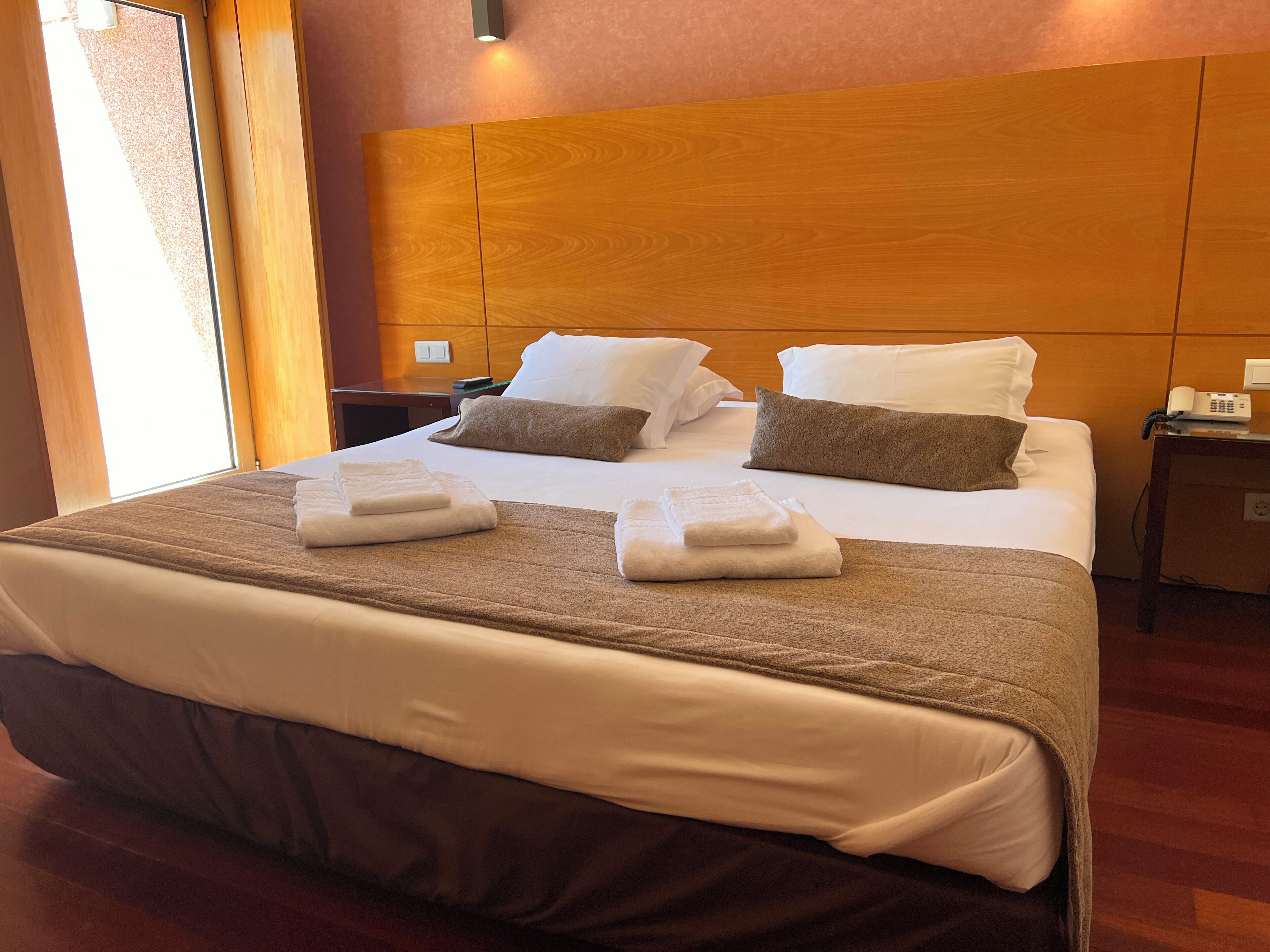 A hotel room with a large bed, wooden headboard, white linens, and two bedside tables with lamps.