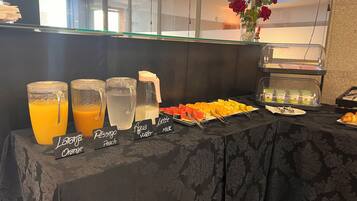 A breakfast buffet with labeled beverages and a variety of fruits and pastries.