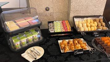 Un bufé con diferentes opciones de comida, incluyendo pasteles, pan y bocadillos envasados.