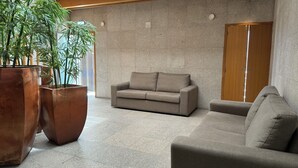 A modern living room with a beige sofa, a large potted plant, and a wooden wardrobe. - Flag Hotel Barcelos (Barcelos)