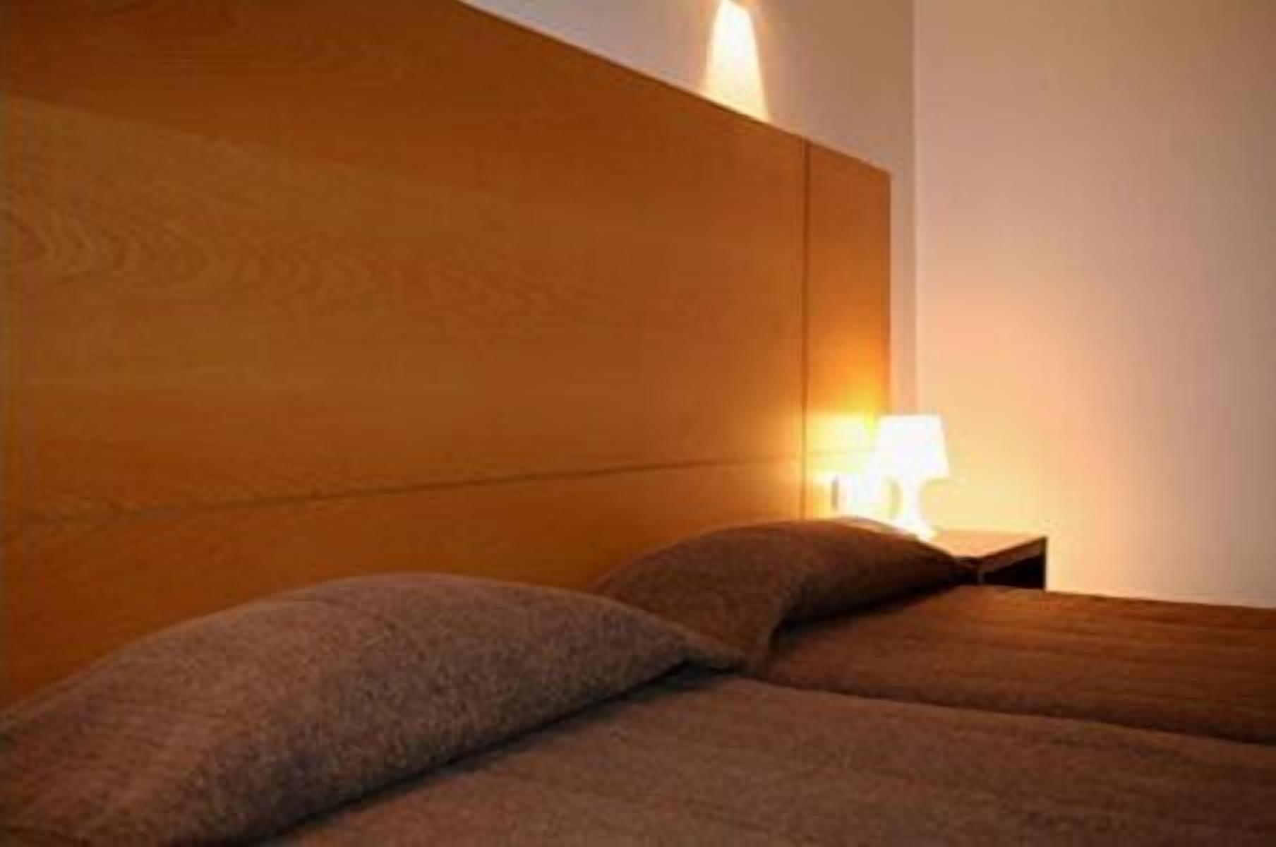 Un dormitorio con cabecera de madera, dos almohadas y una lámpara de noche.
