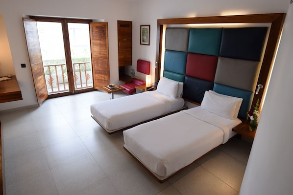 A hotel room with two beds, a balcony, a desk, and a nightstand with a lamp.