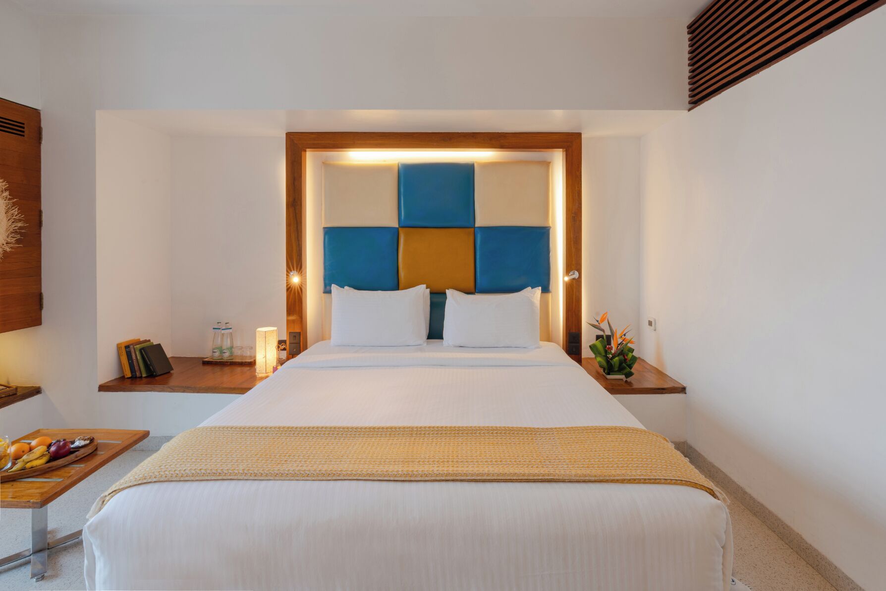 A hotel room with a bed, bedside tables, a nightstand, and a small table with fruit.