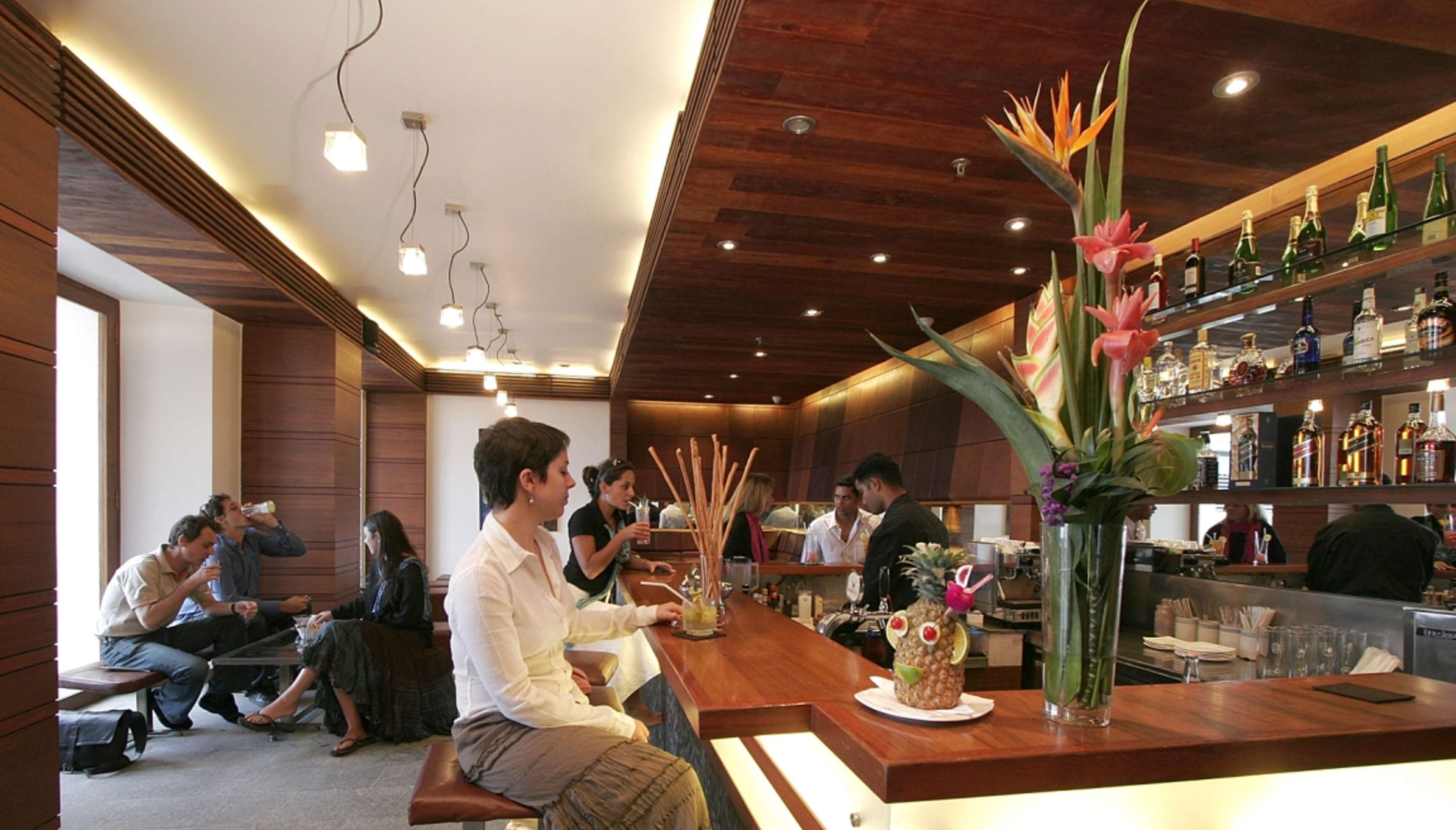 A bar area with wooden paneling, a variety of liquor bottles, and a decorative plant arrangement.