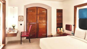 A hotel room with a bed, a desk with a chair, a wardrobe, and a small table with items.