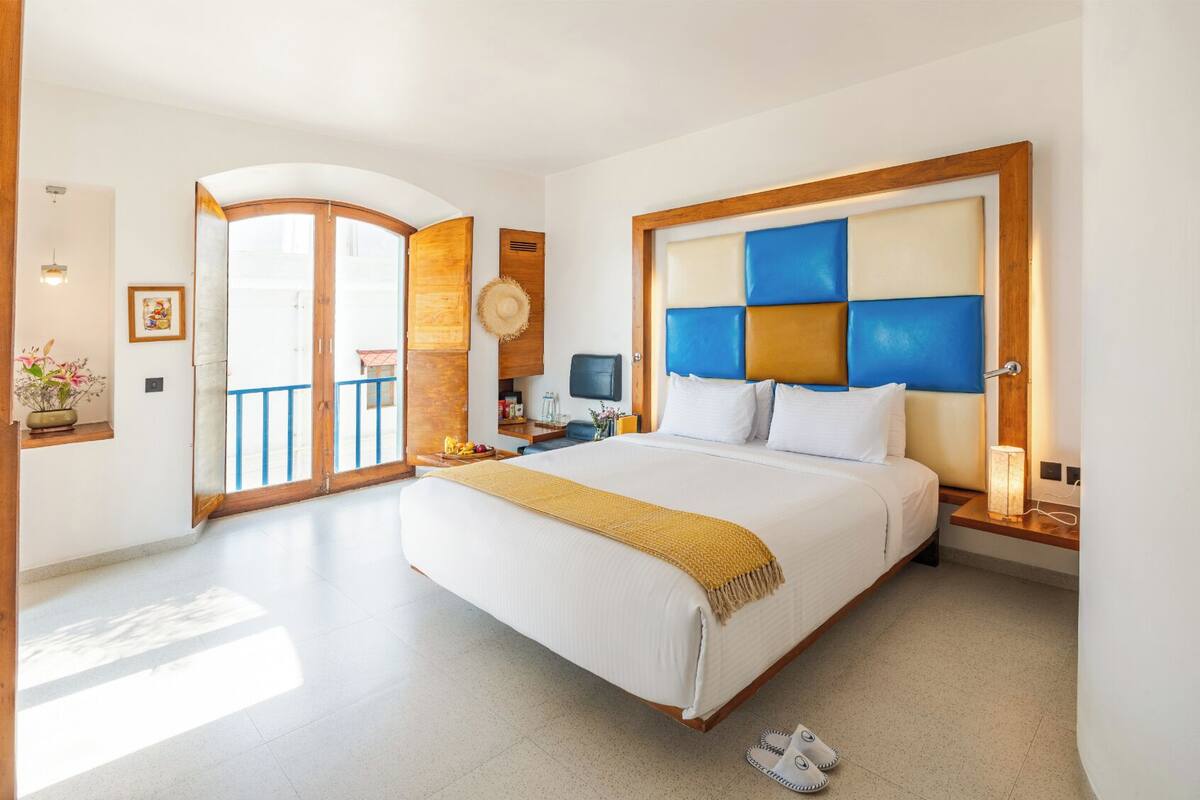 A hotel room with a large bed, a TV, a balcony, and a wooden headboard.