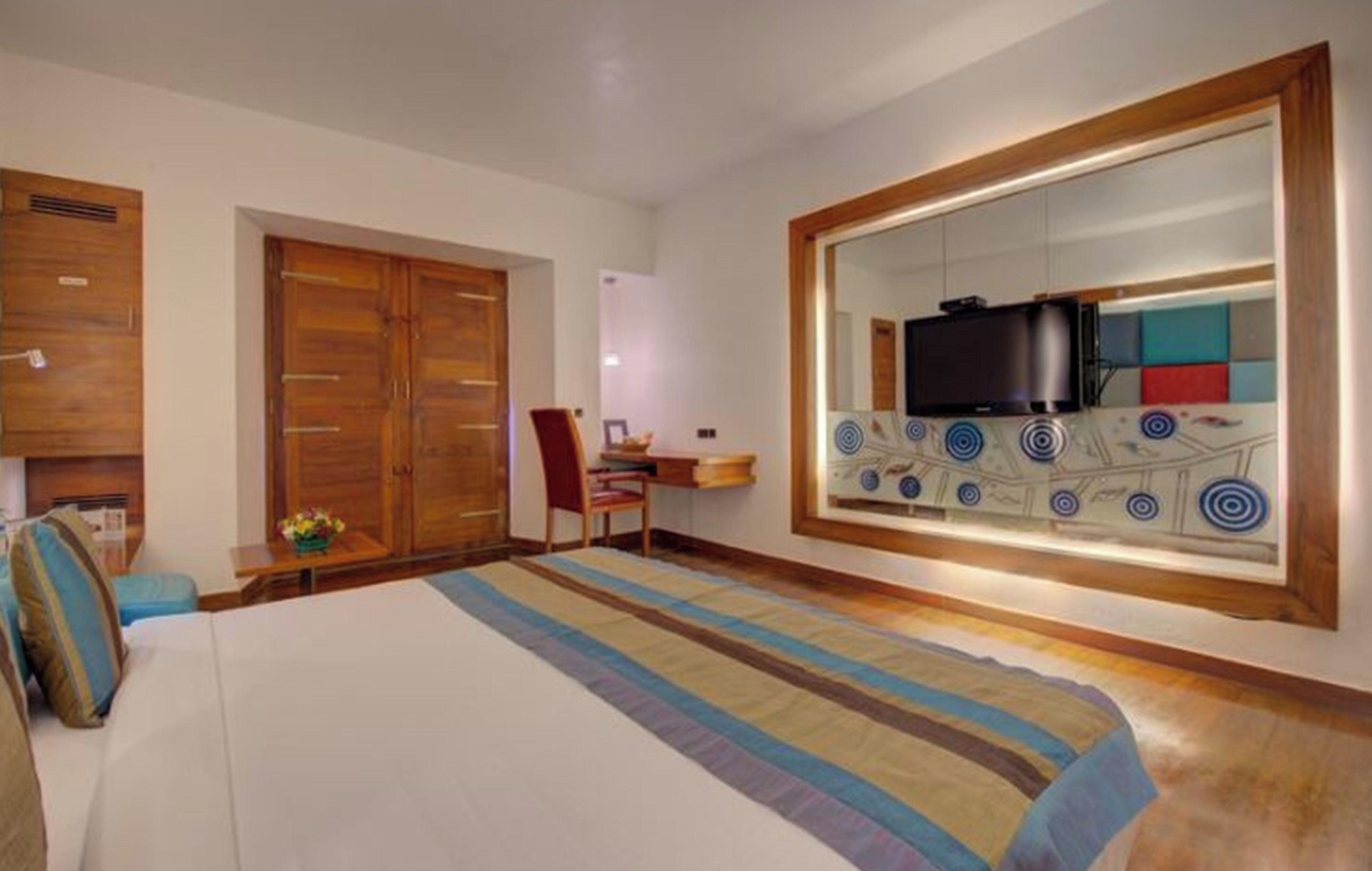 Habitación de hotel con cama, escritorio, silla, armario y un espejo grande con televisor.