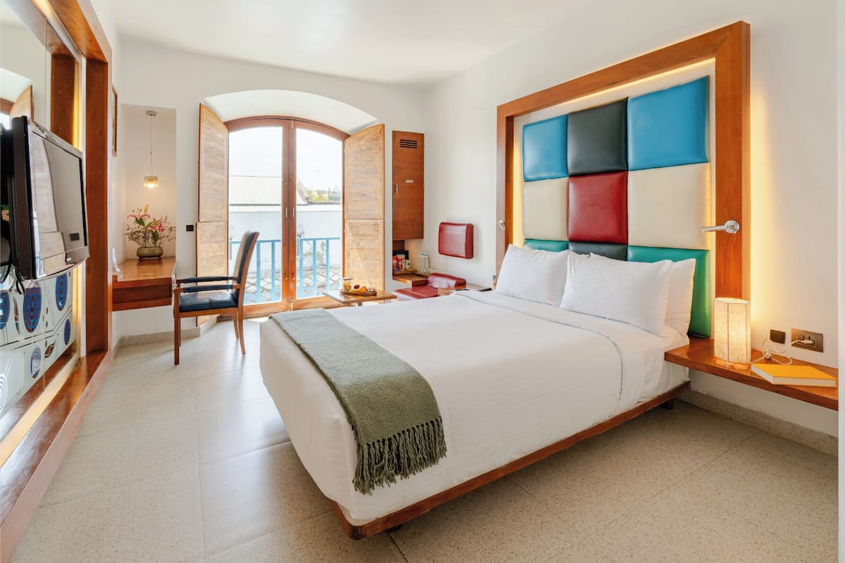 A hotel room with a bed, a desk, a chair, a TV, and a balcony with a view.