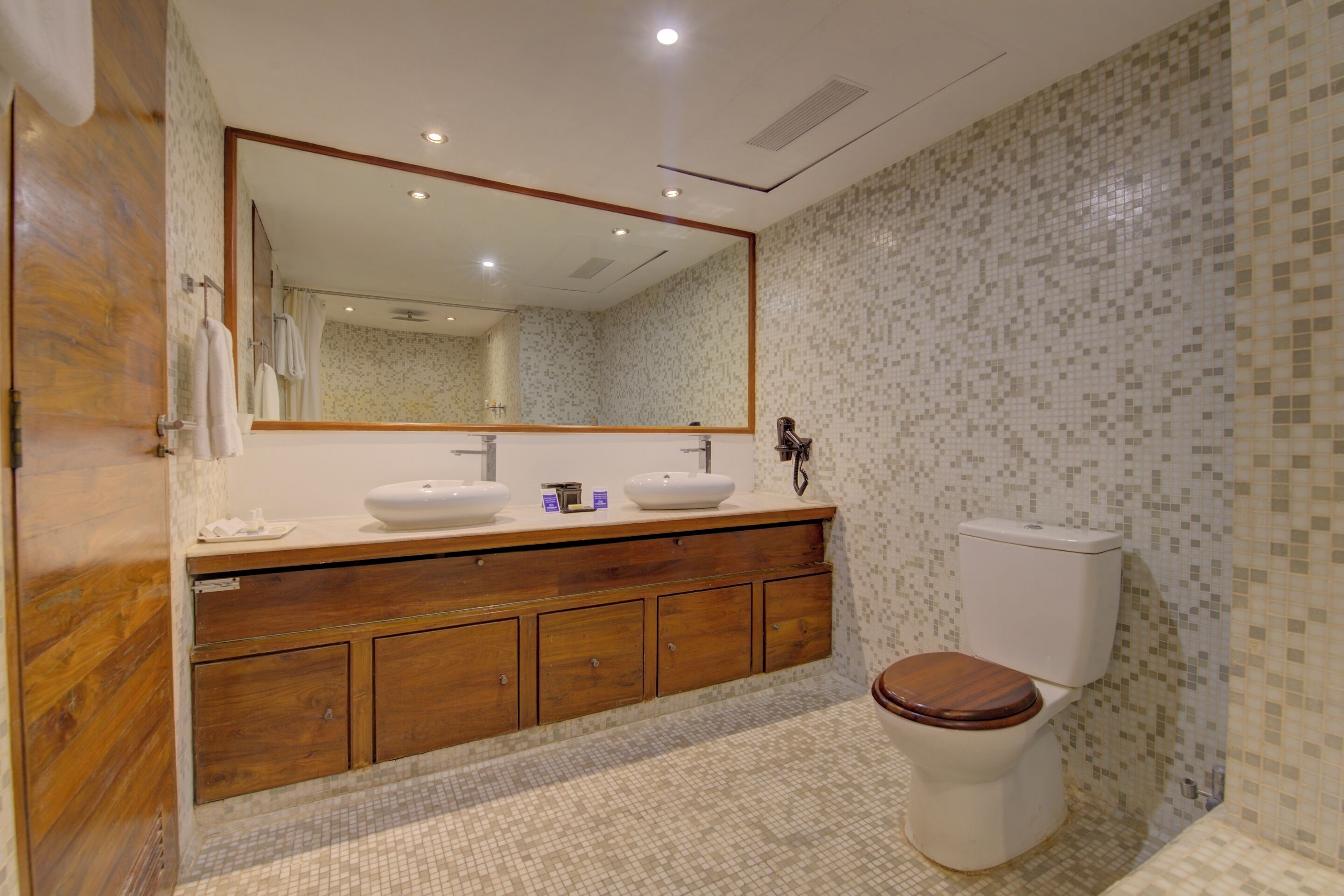 Un bagno con un mobiletto vanità in legno, due lavandini, un water e uno specchio grande.