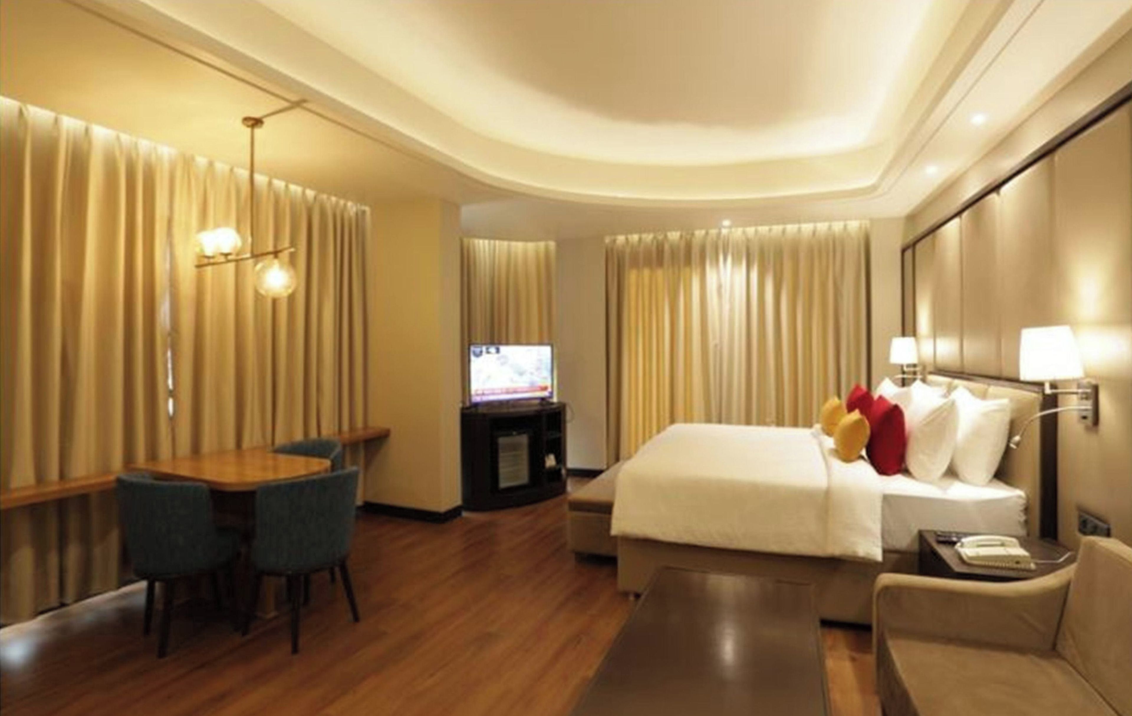 A hotel room with a bed, a desk, a chair, a television, and a sofa.