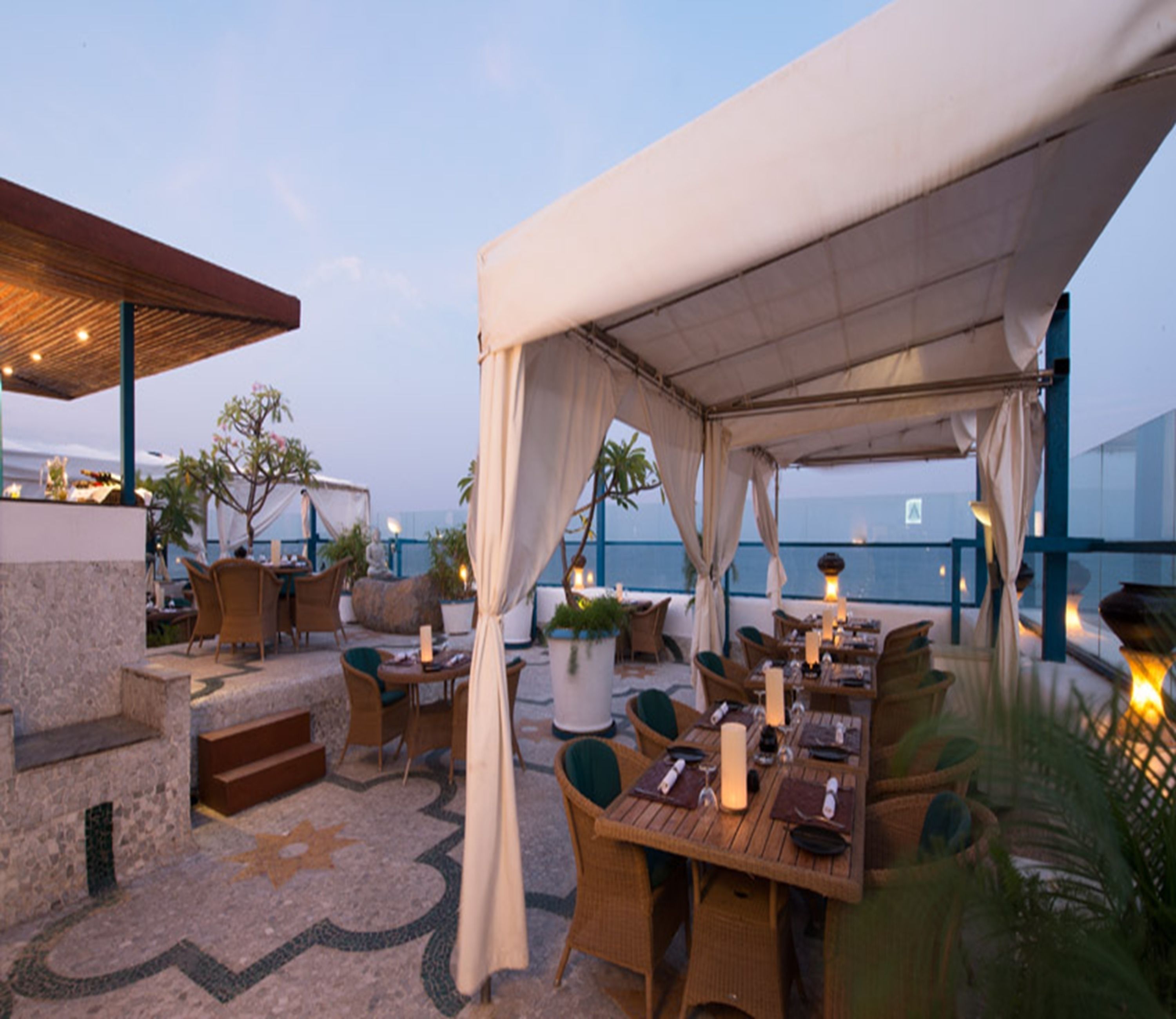 Un espace extérieur aménagé pour les repas, avec des tables et des chaises, un coin salon abrité et une vue sur la mer.