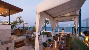 Un espace extérieur aménagé pour les repas, avec des tables et des chaises, un coin salon abrité et une vue sur la mer.