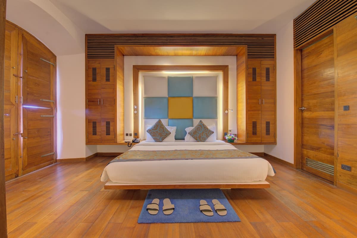 A spacious bedroom with a large bed, wooden wardrobe, and a built-in headboard with a light panel.