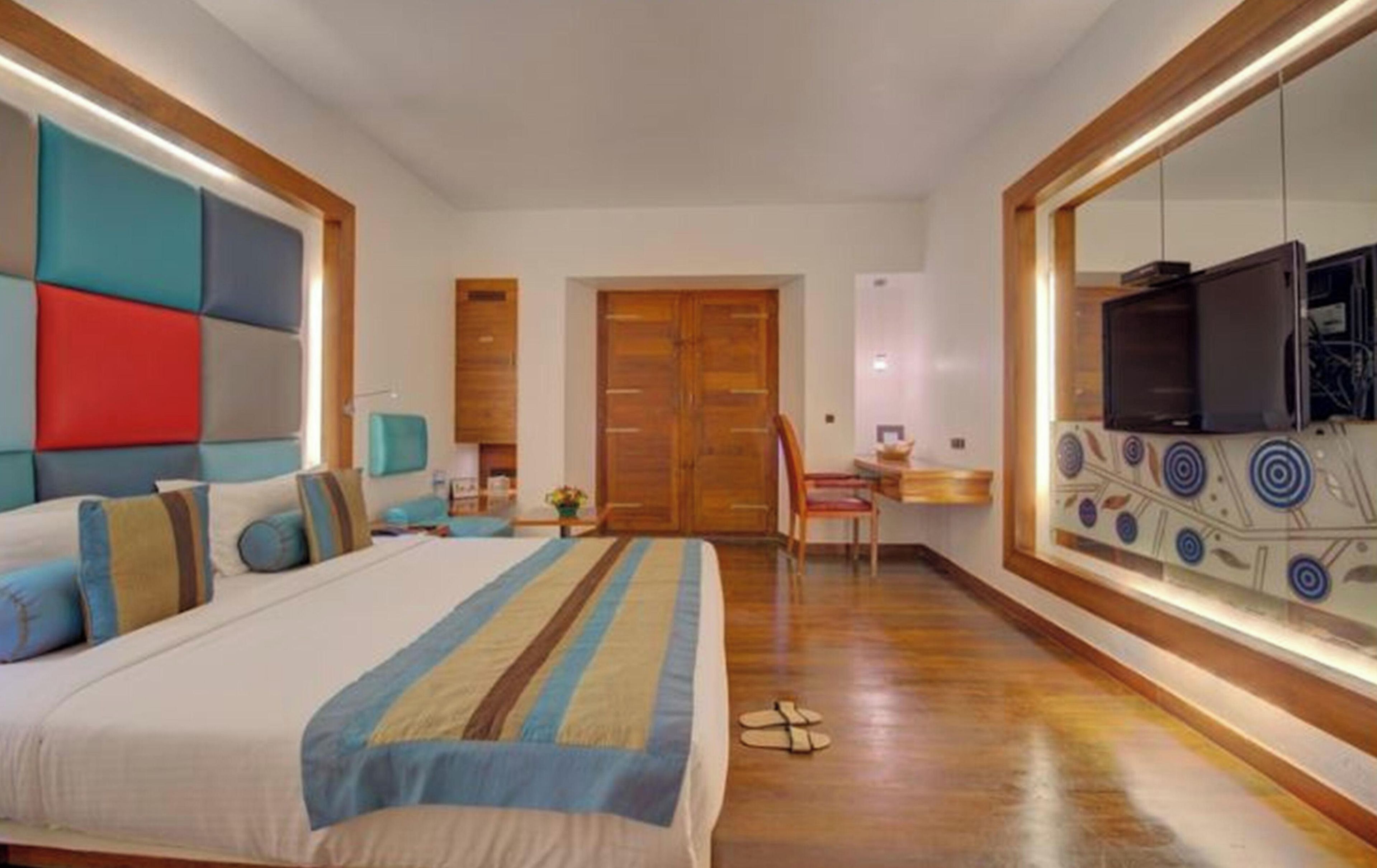 A hotel room with a large bed, a desk, a television, and a mirror.