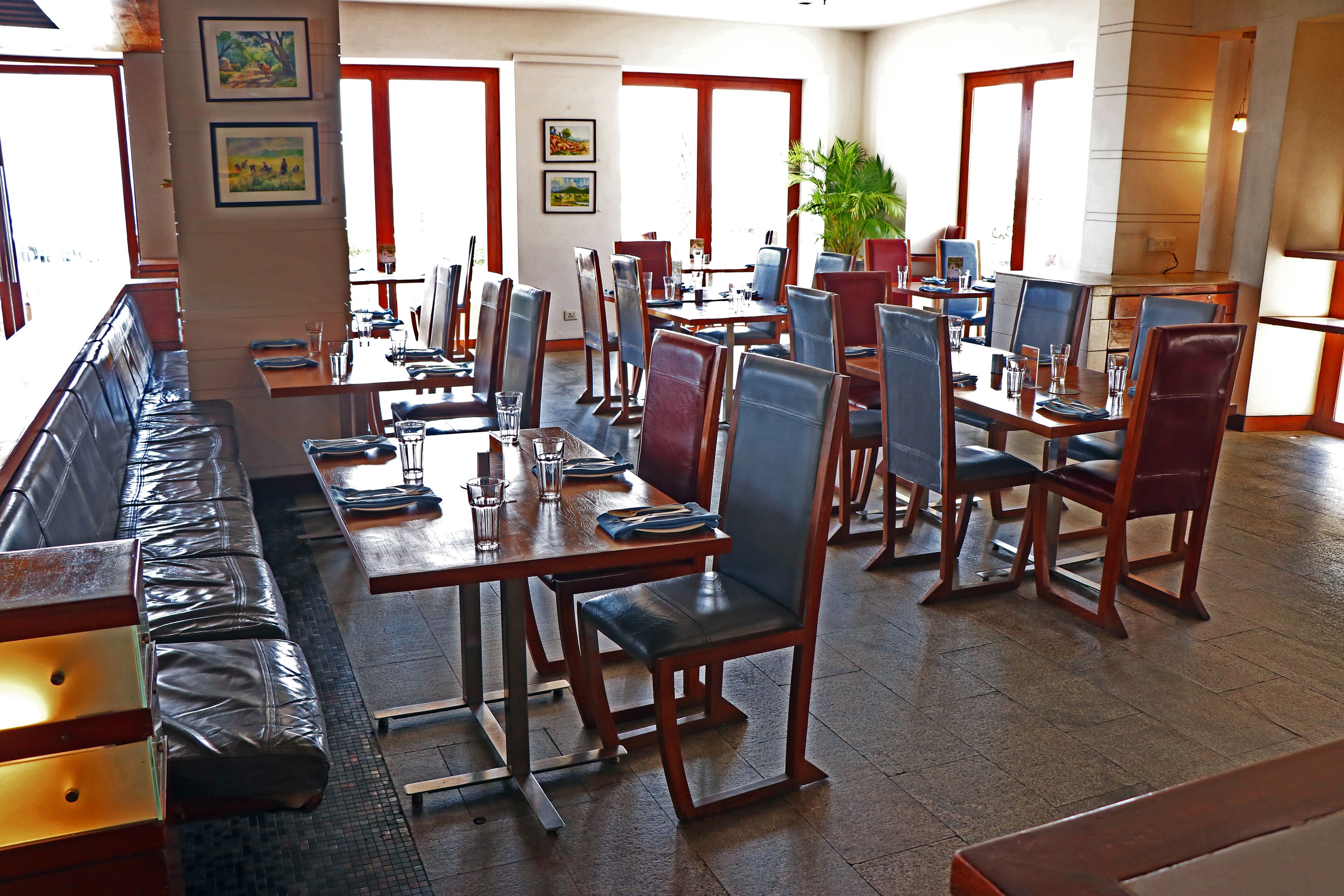 A spacious dining area with multiple tables and chairs, a long bench, and large windows allowing natural light.