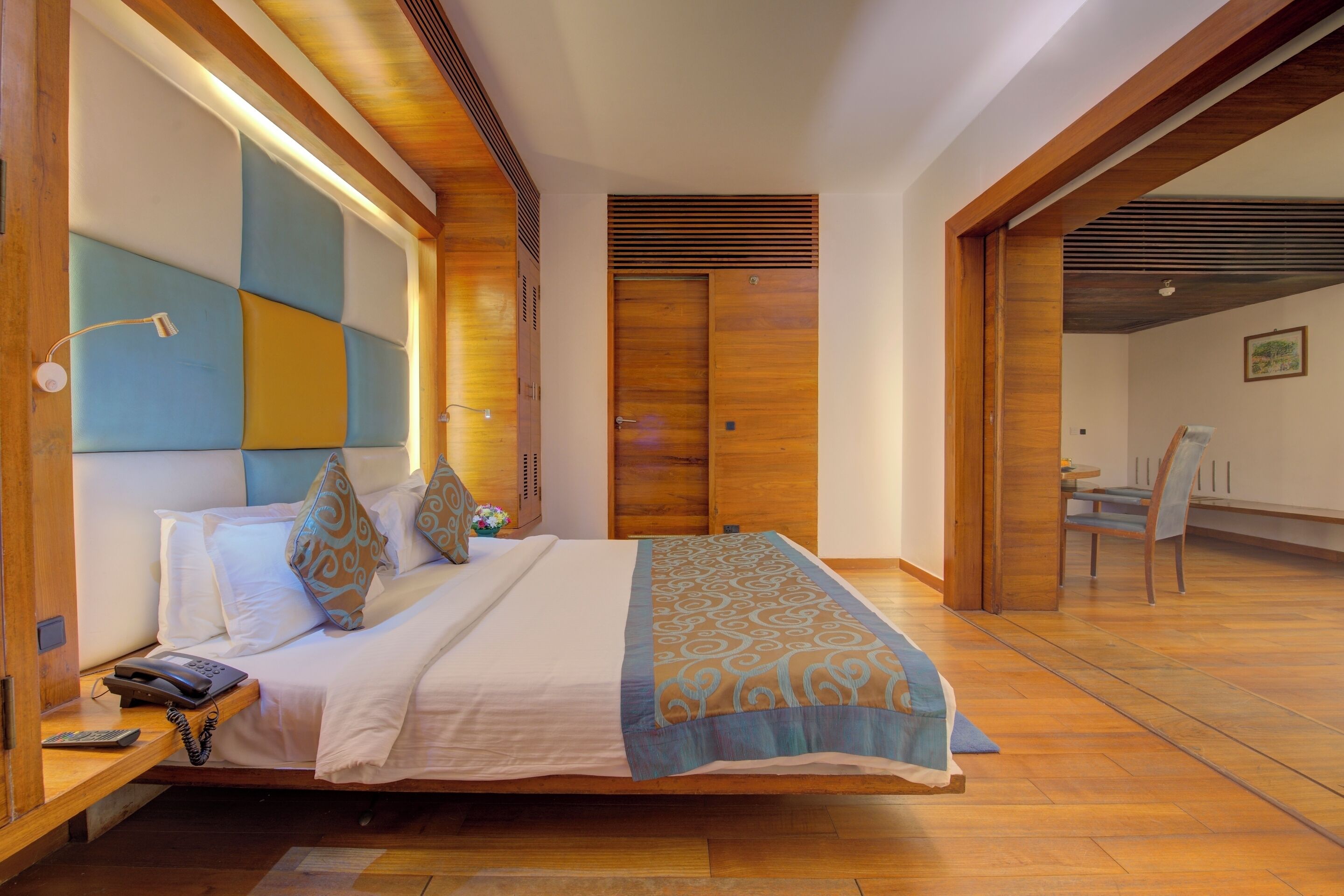 A modern hotel room with a large bed, wooden headboard, and a desk with a telephone.