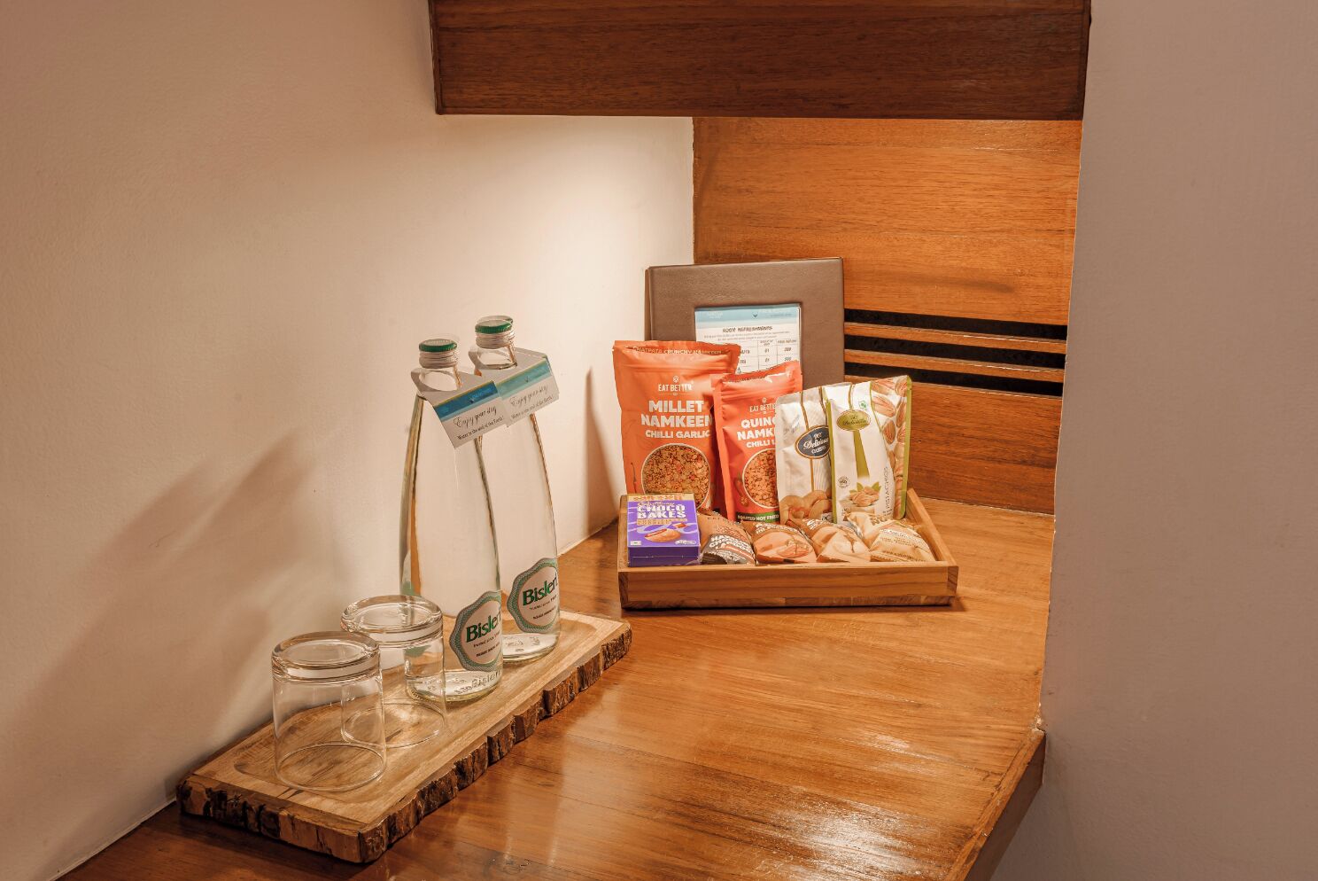 A wooden counter with a glass bottle rack, a tray of snacks, and a framed menu.