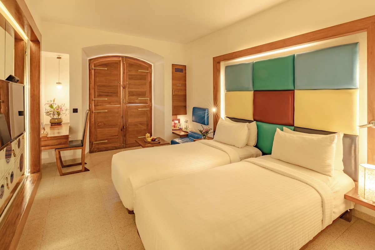A hotel room with two beds, a desk, a wardrobe, and a television.