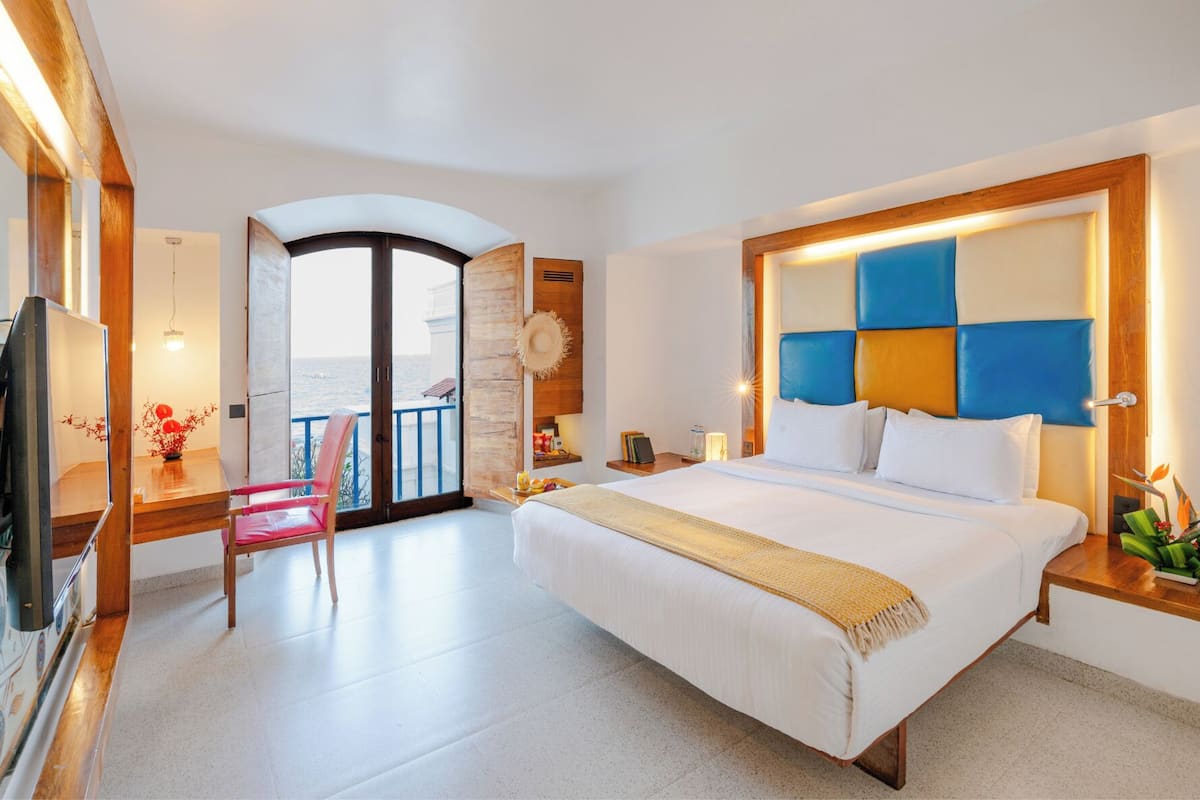 A hotel room with a bed, a desk, a chair, a TV, and a balcony with a view.