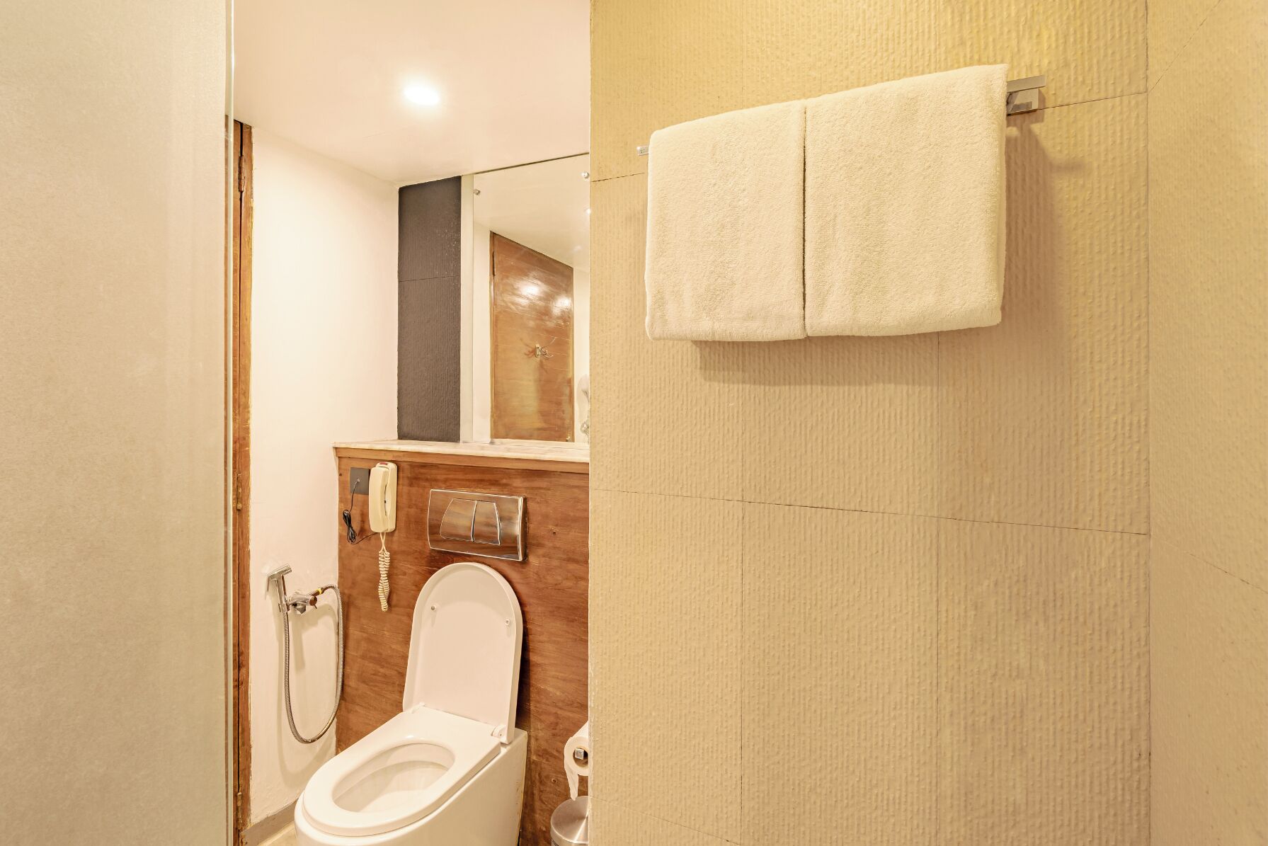 A bathroom with a toilet, a shower, a towel hanging on the wall, and a mirror.