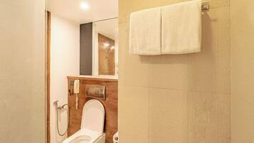 A bathroom with a toilet, a shower, a towel hanging on the wall, and a mirror.