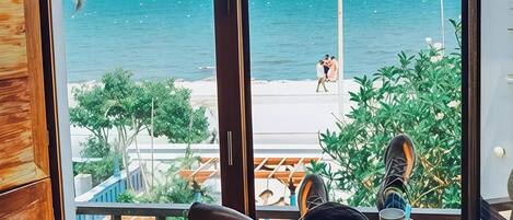 A balcony with a view of the sea, a person relaxing with a drink, and a wooden wall.
