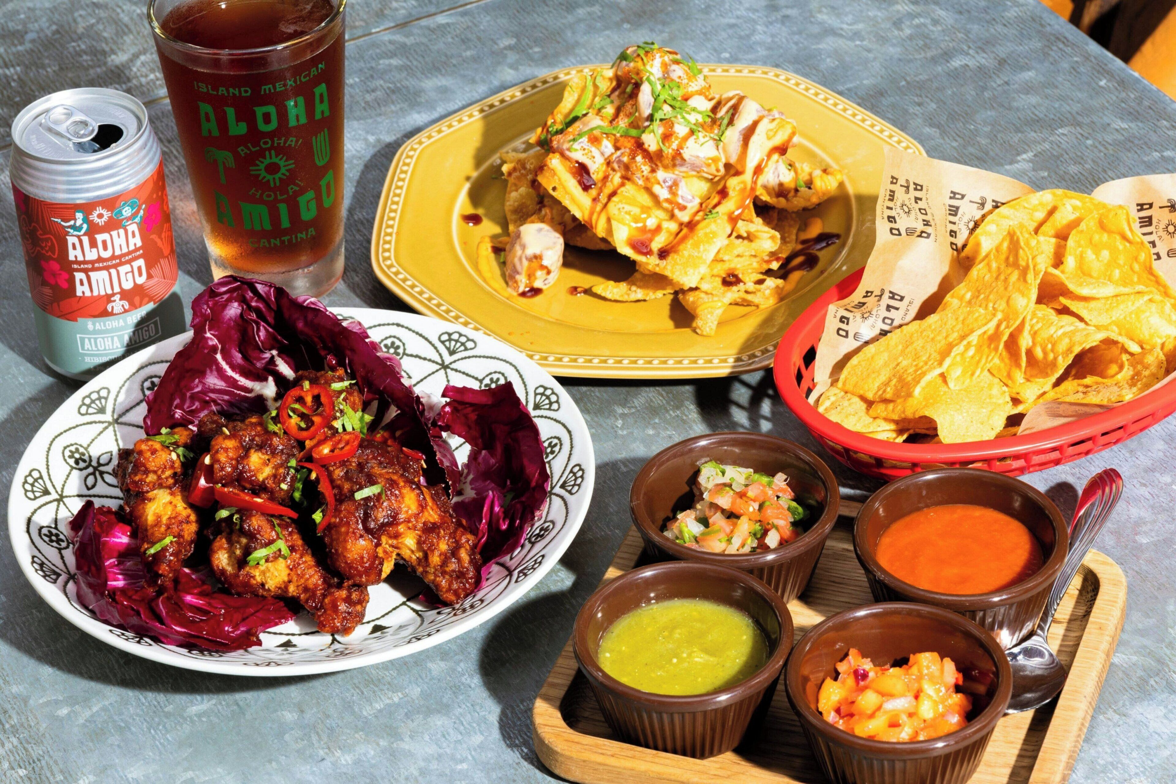 A table with various dishes including a plate of chicken, a bowl of chips, and several small bowls of sauces.
