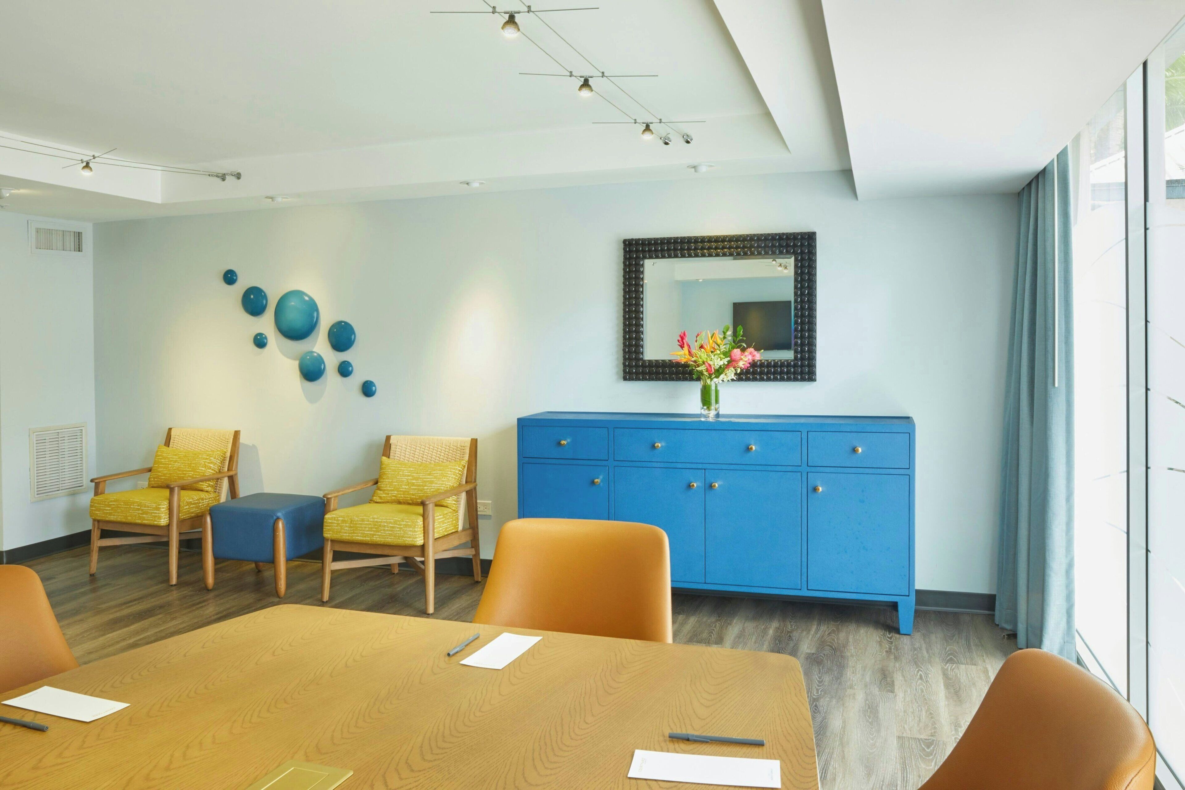 A conference room with a wooden table, yellow chairs, a blue cabinet, and a mirror on the wall.